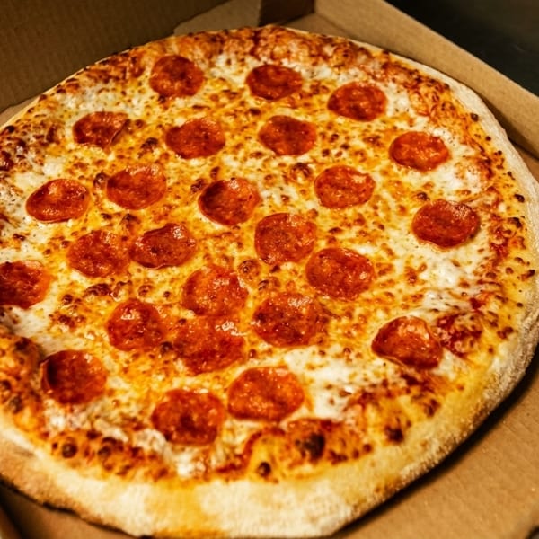 A freshly baked pepperoni pizza with melted cheese sits in an open cardboard delivery box.