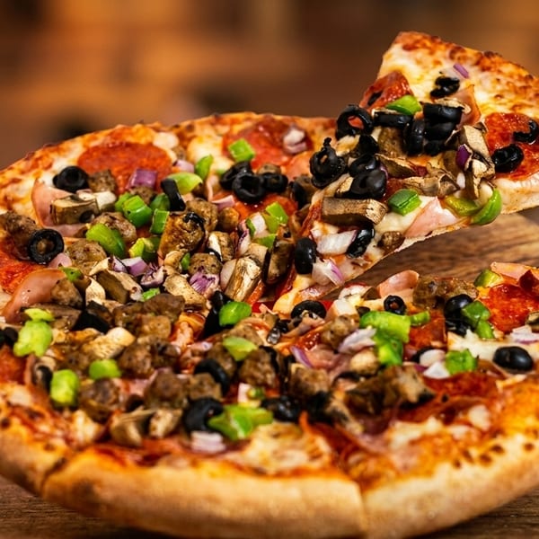 A slice of supreme pizza, topped with pepperoni, olives, and green peppers, being lifted from the pie.